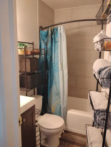 White vanity with a solid surface countertop, wood-finish flooring, and a tiled shower surround