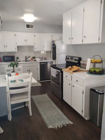 White cabinetry with stainless steel appliances, dark wood-finish flooring, and a white tile backsplash