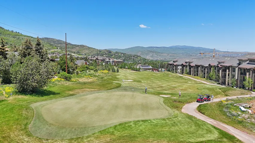 Expansive green space featuring a golf course putting green with flag, surrounded by lush landscaping and a paved cart path