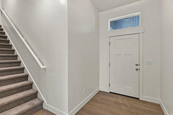 Entryway with wood-finish flooring, a white paneled door with transom window, and a carpeted staircase with white handrail