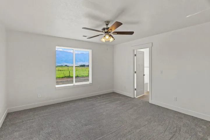 Carpeted room with a ceiling fan, a window featuring a natural landscape, and a white interior door