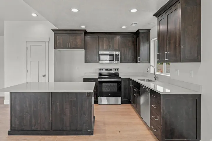 Kitchen featuring dark wood-finish cabinetry, light-toned countertops, stainless steel appliances, and a central island