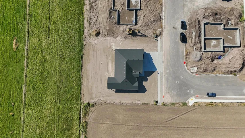 Property featuring a dark-toned roof, concrete driveway, and an adjacent undeveloped lot