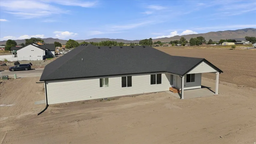 Newly constructed residence featuring light-colored siding, a dark shingle roof, and a covered back patio with support columns