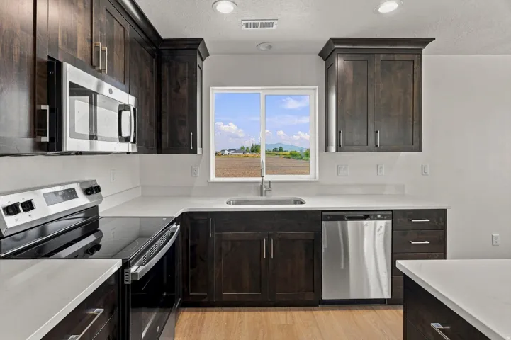 Kitchen featuring wood-finish cabinetry, stainless steel appliances, light-toned countertops, and a window above the sink