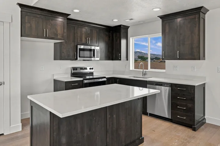 Kitchen featuring dark wood-finish cabinetry, light countertops, a kitchen island, stainless steel appliances, and a stainless steel sink