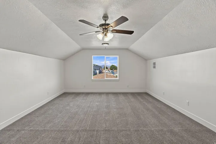 Spacious room with sloped ceilings, a window, and an overhead ceiling fan with integrated lighting