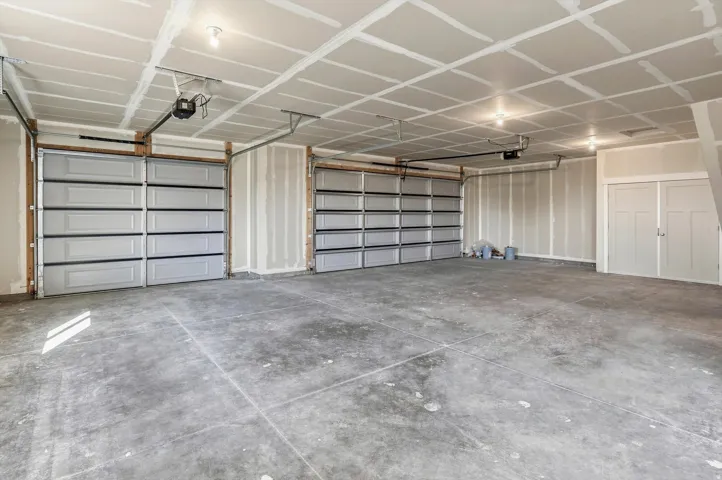 Large garage space with two overhead doors, overhead lighting, and concrete flooring