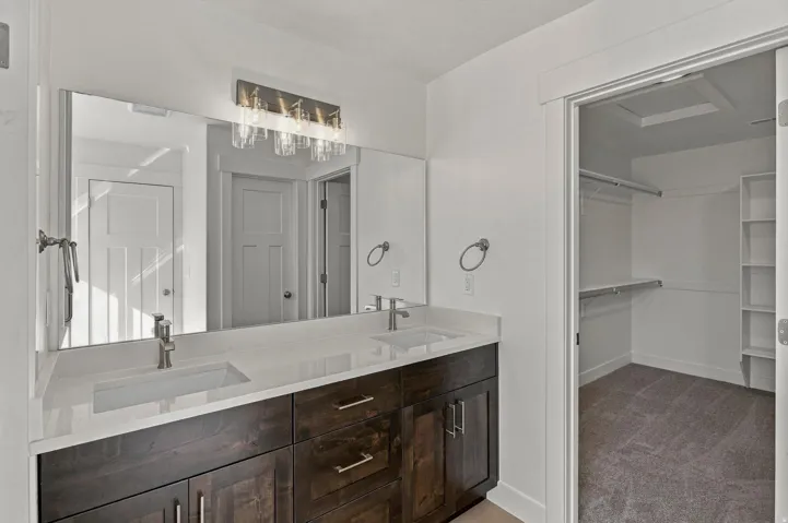 Dual vanity with integrated sinks, wood-finish cabinetry, a large wall-mounted mirror, and decorative wall sconce