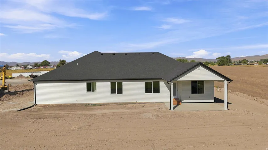 Newly constructed residence featuring a covered patio, multiple windows, and a dark shingle roof