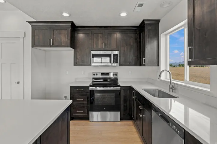Dark wood-finish cabinetry, stainless steel appliances, light-toned countertops, and wood-finish flooring