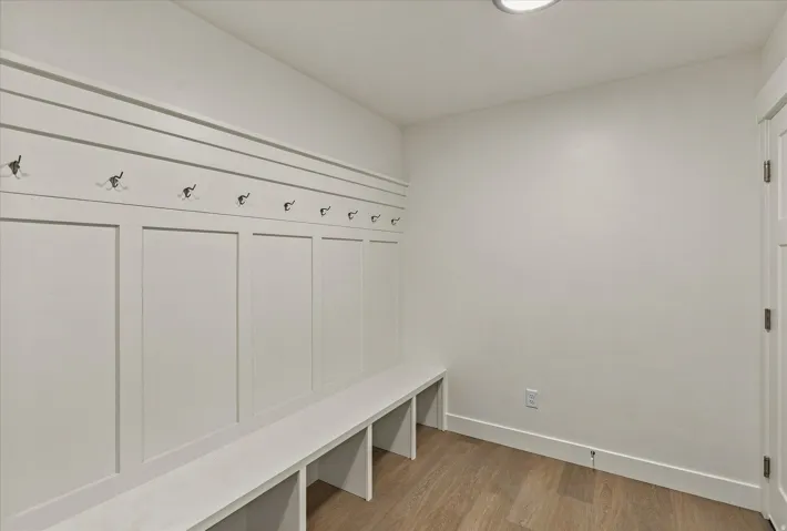 Integrated mudroom bench with storage cubbies, decorative board and batten wall treatment, array of wall-mounted hooks, and wood-finish flooring