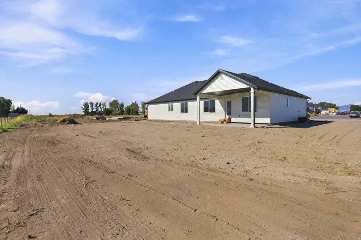 New construction residence featuring a covered patio, dark shingle roof, and light-toned siding