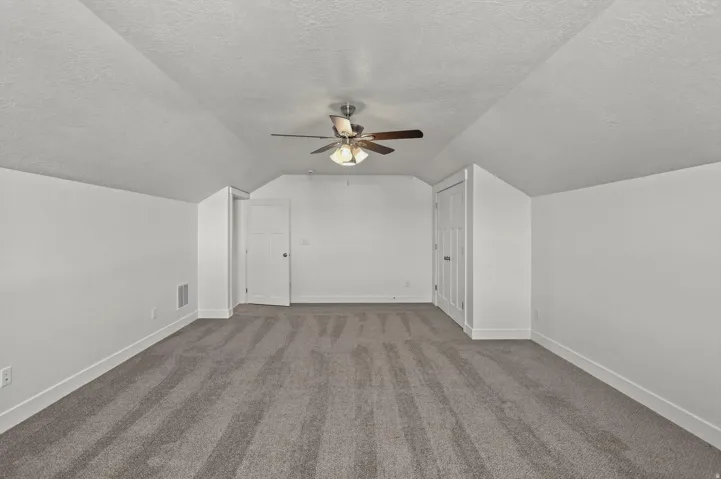 Spacious room featuring sloped ceilings, plush gray carpeting, and a ceiling fan with integrated lighting