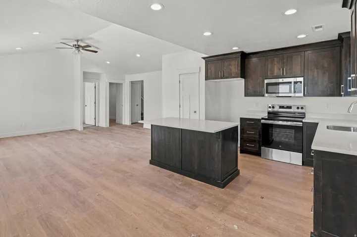 Vaulted ceiling with recessed lighting, dark wood-finish cabinetry, stainless steel appliances, large kitchen island with white countertop, and wood-finish flooring