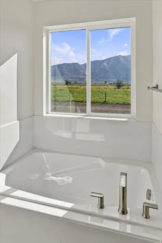 Recessed soaking tub with deck-mounted brushed nickel fixtures, surrounded by white stone-finish tile