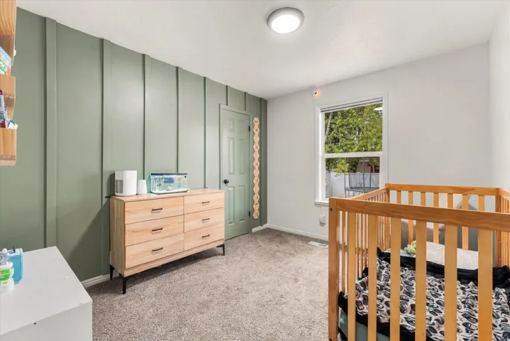 Wall-to-wall carpeting with a board and batten accent wall, recessed ceiling light, and a window providing natural illumination