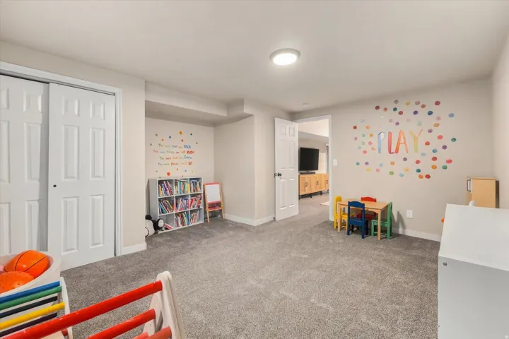 Recessed lighting illuminates a spacious room featuring neutral-toned carpeting, white trim, and a white six-panel door