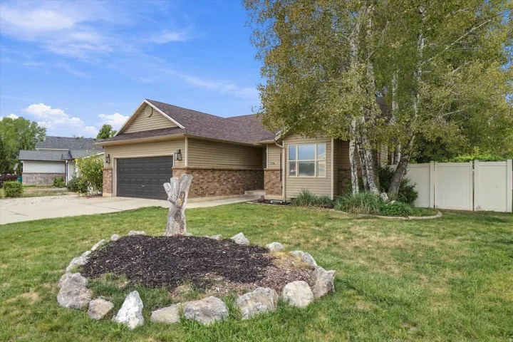 Exterior featuring horizontal siding, brick accents, an attached garage, a paved driveway, and a white privacy fence