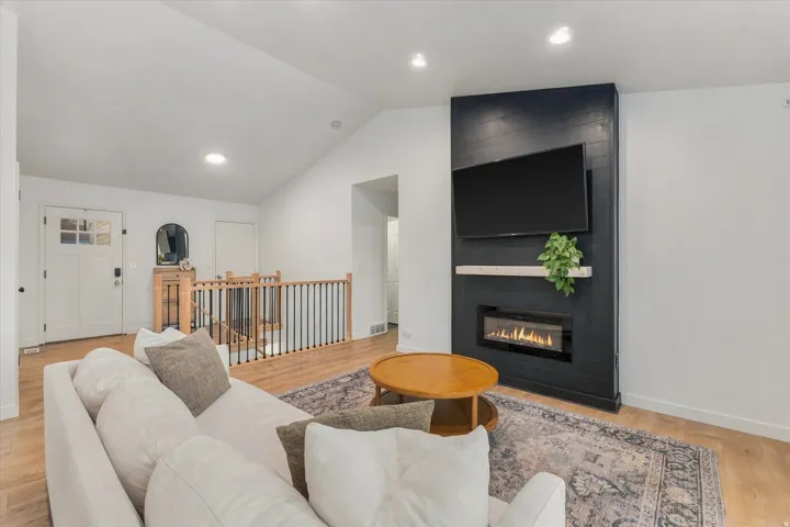 Vaulted ceiling, wood-finish flooring, white walls, black accent wall with built-in fireplace, and a black metal and wood railing