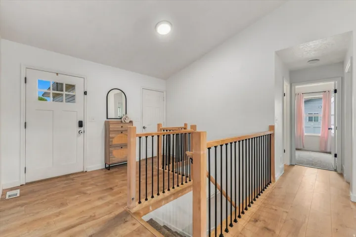 Light wood-finish flooring throughout, white interior walls, and a staircase featuring wood handrails and black metal balusters