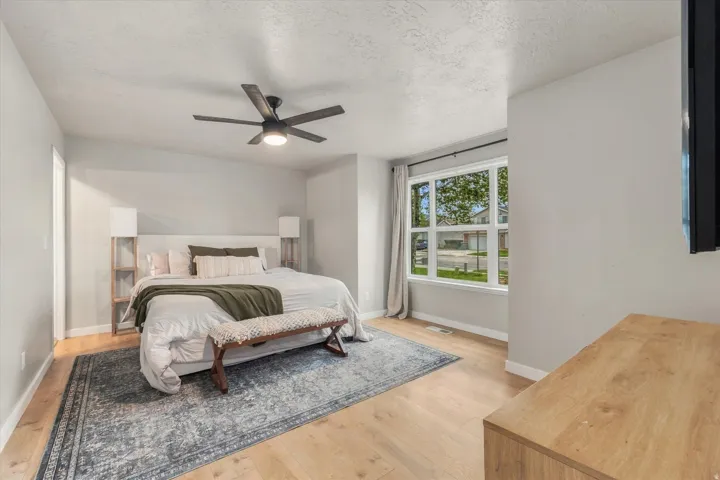 Spacious room with wood-finish flooring, a contemporary ceiling fan, and ample natural light from a large window