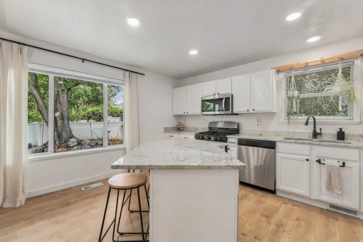 Kitchen featuring white cabinetry, light-toned countertops, stainless steel appliances, and wood-finish flooring