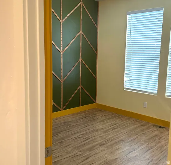 Decorative accent wall with geometric wood trim, two windows with blinds, and wood-finish flooring