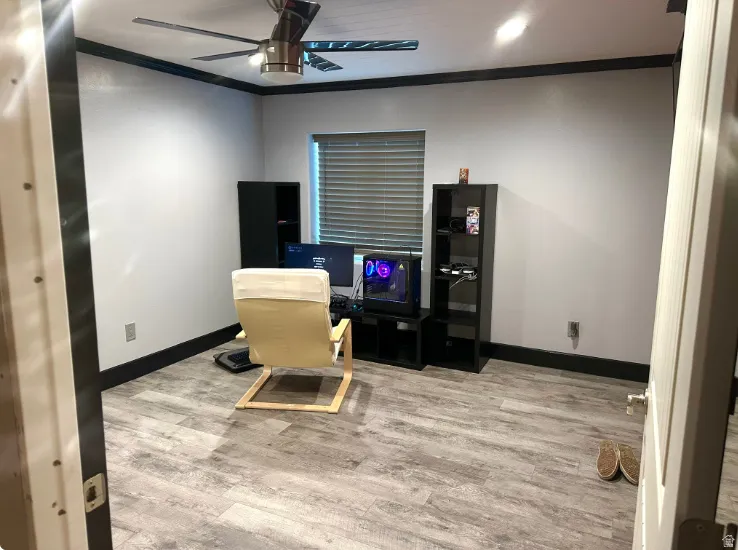 Wood-finish flooring with dark trim, ceiling fan with light fixture, and window with blinds