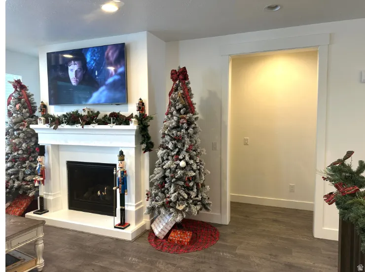 Christmas time. White mantel with a black hearth, wood-finish flooring, and a cased opening