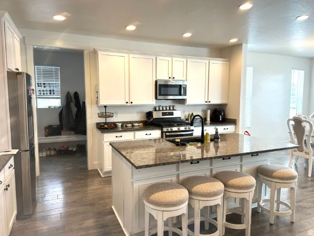 Kitchen featuring white cabinetry, stainless steel appliances, recessed lighting, and an island with a stone-finish countertop