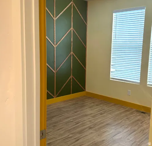 Decorative accent wall with geometric wood trim, two windows with blinds, and wood-finish flooring