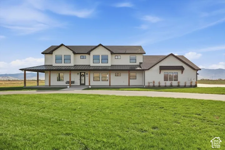 Modern farmhouse exterior featuring white siding, a dark metal roof accent, a covered front porch with wood columns, and an expansive front lawn