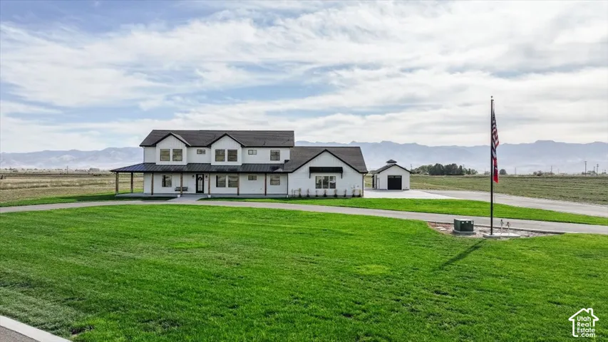 Modern farmhouse exterior with white siding and black trim, featuring a covered porch, detached garage, and expansive green lawn