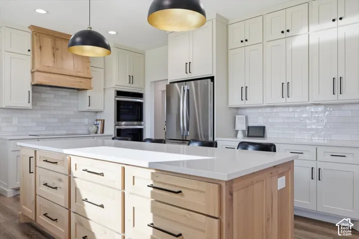 Spacious kitchen featuring a large island with light wood cabinetry, white countertops, stainless steel appliances, and a subway tile backsplash