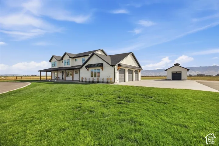 Modern farmhouse exterior with a covered porch, three-car garage, and a detached auxiliary building