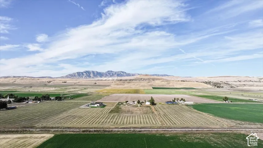 Expansive agricultural landscape with cultivated fields, scattered residential structures, and distant mountains