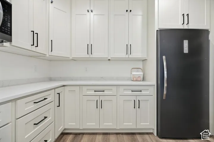 White shaker-style cabinetry with matte black hardware, light-toned countertops, wood-finish flooring, and a built-in microwave