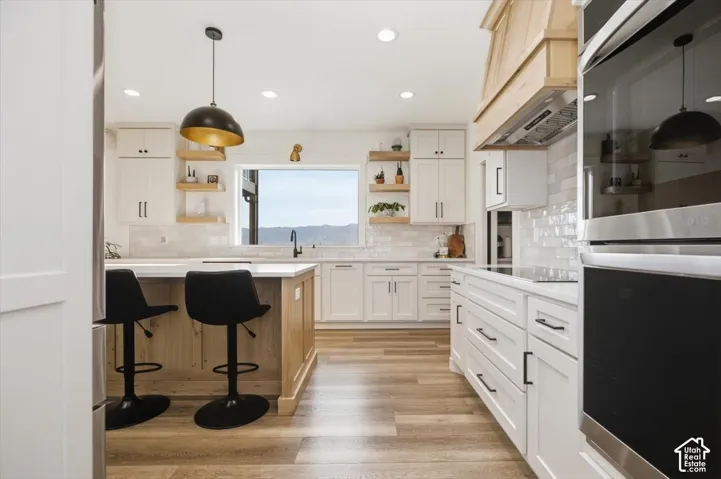 Contemporary kitchen featuring white cabinetry, wood-finish flooring, a central island with natural wood paneling, a large window, and stainless steel appliances