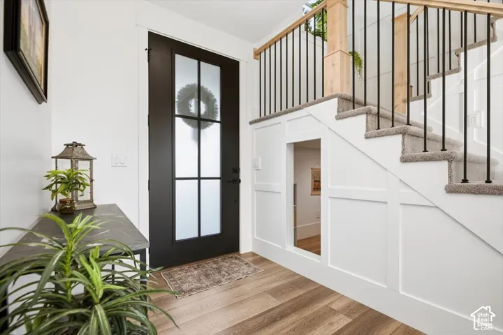 Frosted glass panel entry door, wood-finish flooring, carpeted staircase with dark metal spindles, natural wood handrail, and custom under-stair alcove