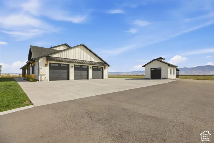 Modern farmhouse exterior with board and batten siding, three-car garage, covered porch, detached outbuilding, and expansive paved driveway