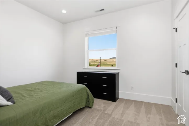 Recessed ceiling lighting, white walls, window with a window blind, carpeted flooring, and a white paneled door with dark hardware