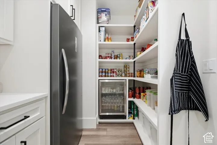 Built-in shelving, wood-finish flooring, integrated beverage cooler, full-size refrigerator, and white cabinetry with dark hardware