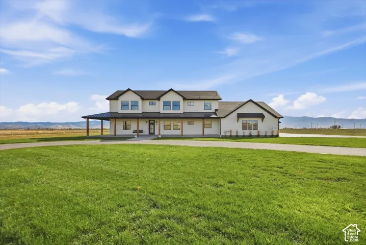 White exterior with black trim, a covered porch with exposed wood posts, a dormer window, and an expansive lawn