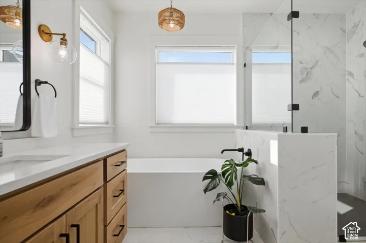 Freestanding soaking tub, wood-finish vanity with countertop, glass-enclosed shower with tiled walls, and dual windows