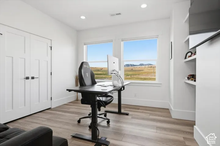 Room with wood-finish flooring, two large windows, white walls, and built-in shelving