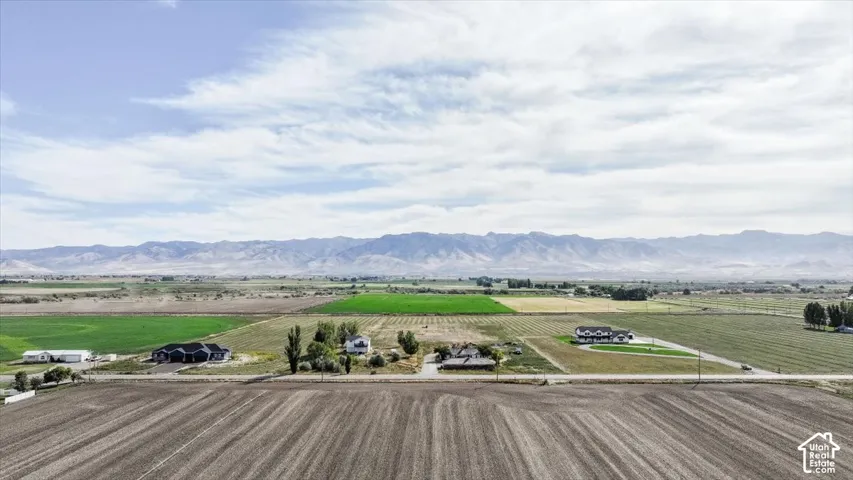 Expansive agricultural landscape with cultivated fields, scattered residential structures, and distant mountain ranges