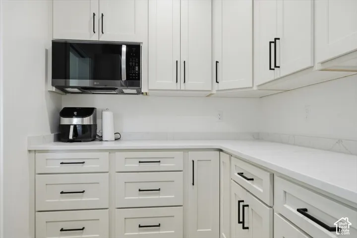White shaker cabinetry with matte black hardware, light-toned countertops, and a built-in stainless steel microwave