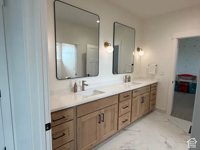 Dual vessel sinks set into a vanity with natural wood-finish cabinetry, black hardware, and quartz countertops