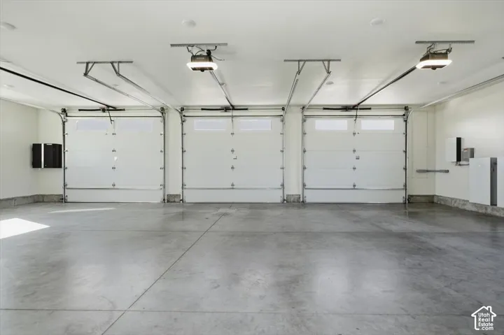 Three white garage doors with automatic openers, concrete flooring, and white walls